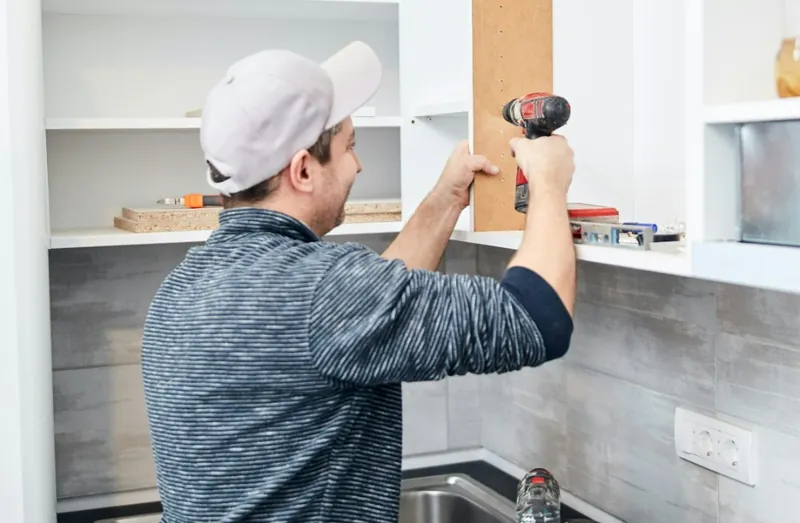 Handyman assembling a wooden cabinet with a power drill