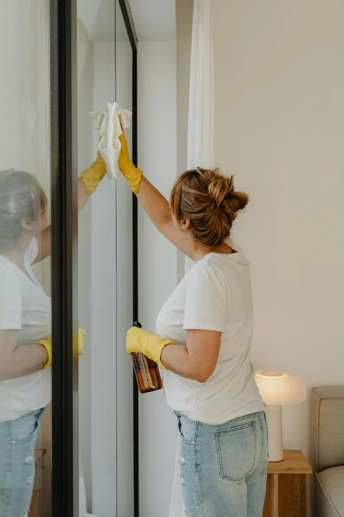 Cleaner in yellow gloves polishing a streak-free glass mirror in an Austrian apartment