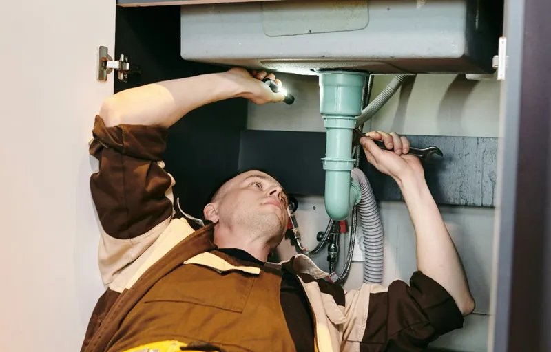 Plumber repairing the siphon under a kitchen sink in Austria