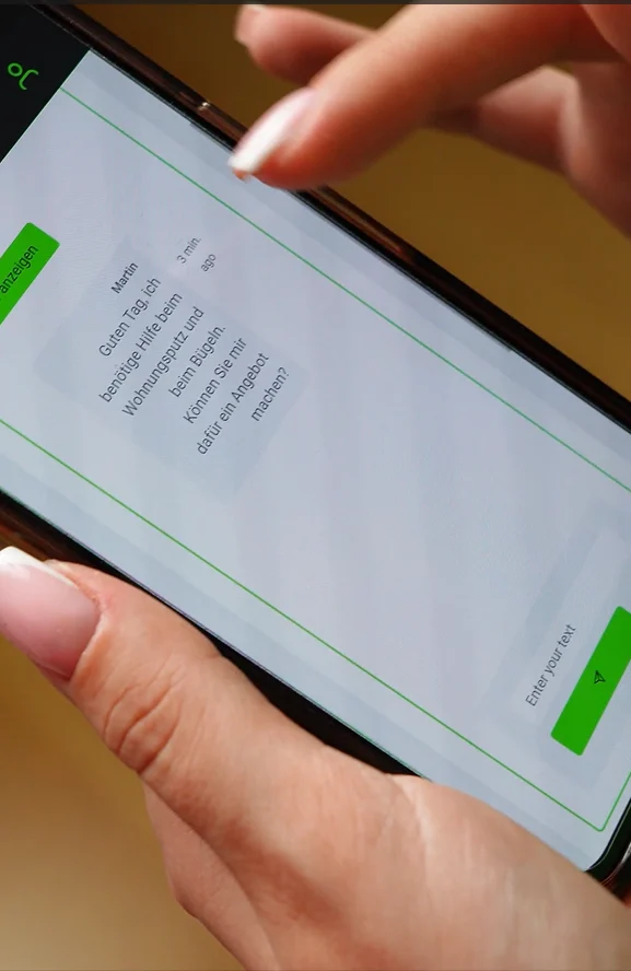 Close-up of hands holding a phone showing a servi.co chat about cleaning and ironing help in German.